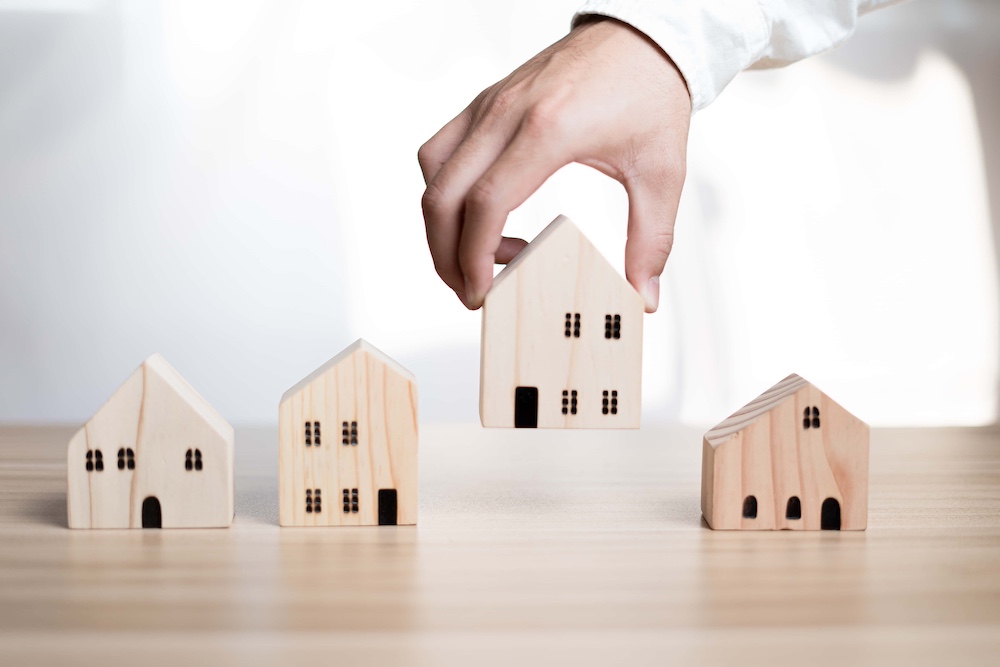 A businessman holding a wooden house placed on a table