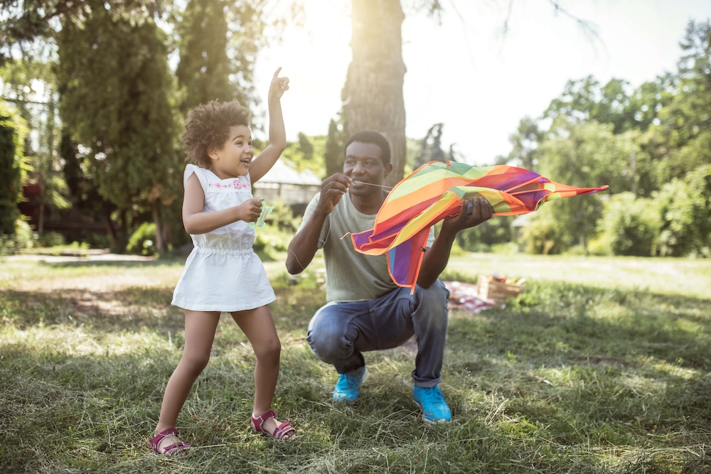 Dark skinned man showing to his kid how to play with the kite