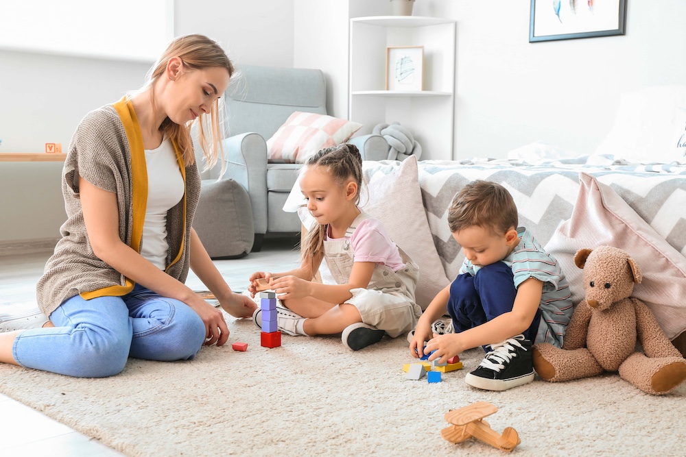 Nanny and cute little children playing at home