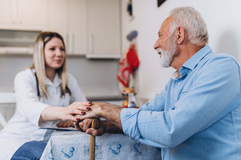 Young positive caregiver taking care of senior man in nursing home